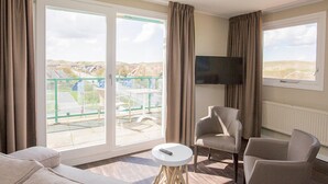 Een hotelkamer met balkon, een televisie en twee fauteuils.