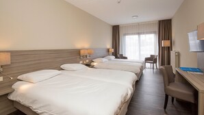 Une chambre d’hôtel avec trois lits, un bureau, une chaise et un téléviseur.