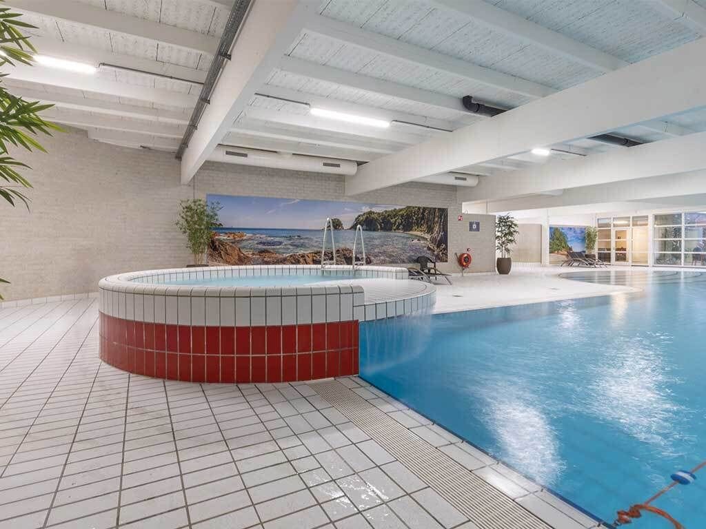 Piscina interna com hidromassagem, piso cerâmico e um mural com cena de praia.