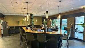 Una zona de bar moderna con una barra alargada, varios taburetes, iluminación colgante y vistas al exterior a través de amplios ventanales.