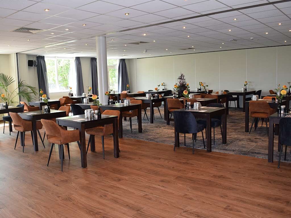 Un comedor amplio con varias mesas y sillas, ventanas grandes con cortinas y piso de madera.
