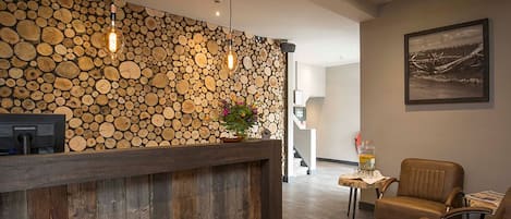 Een receptiegedeelte met een houten wand van boomstammen, een receptiebalie, lederen fauteuils en een ingelijst schilderij.