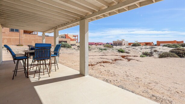 Eine Terrassenanlage im Freien mit Tisch und St ühlen, einem Betonboden und Blick auf eine Wüstenlandschaft mit Gebäuden im Hintergrund.