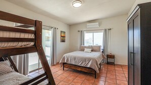 Ein Schlafzimmer mit Etagenbett, einem Einzelbett, einem kleinen Nachttisch, einem Kleiderschrank und einem Fenster mit Vorhängen.