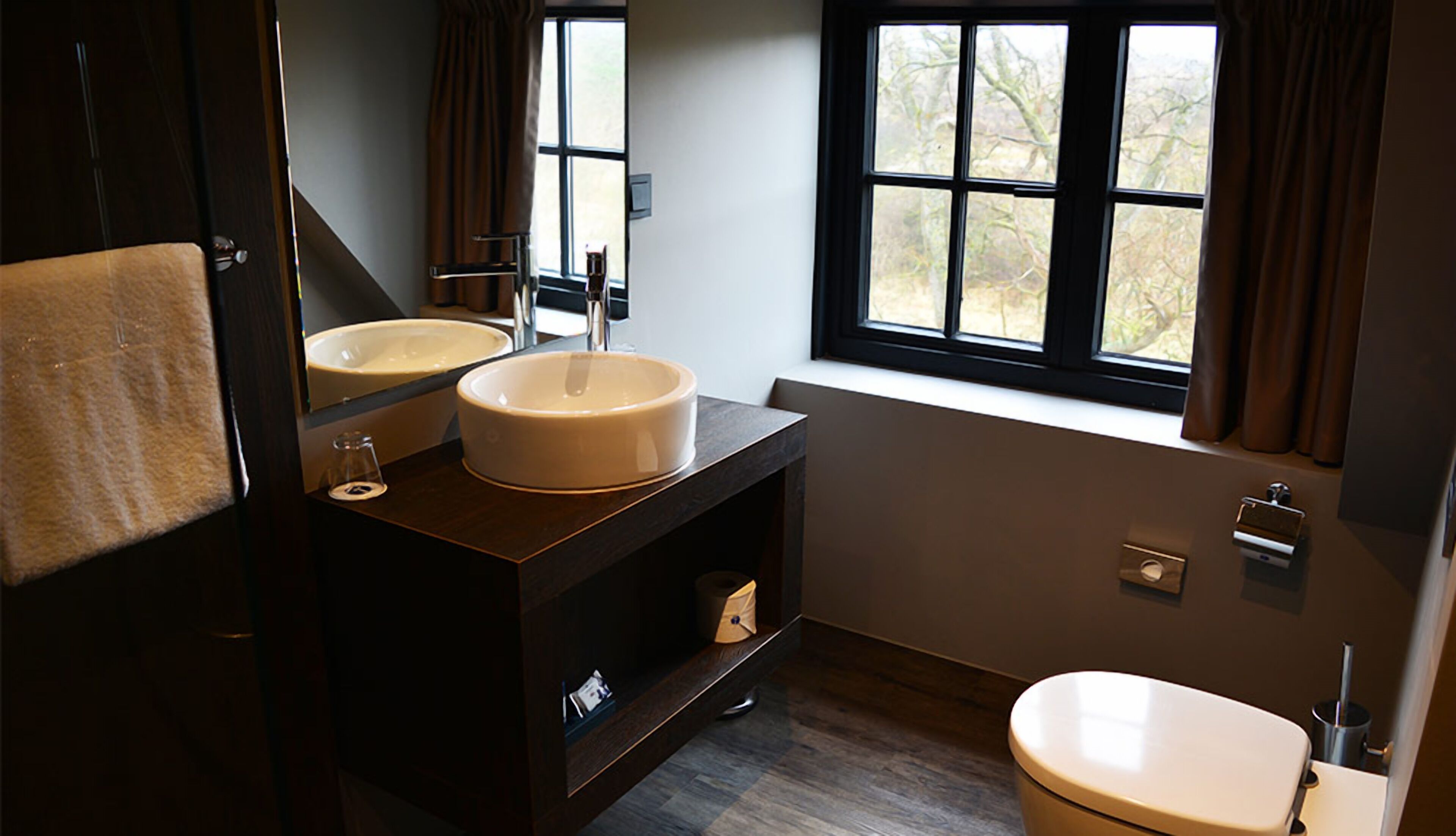 A modern bathroom with two sinks, a toilet, and a window with curtains.