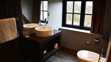 A modern bathroom with two sinks, a toilet, and a window with curtains.