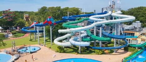 A water park with multiple water slides, a swimming pool, and a sandy area with lounge chairs.