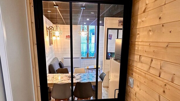 Una stanza con rivestimenti in legno e una porta a cornice nera che dà su un'area pranzo con tavolo e sedie.