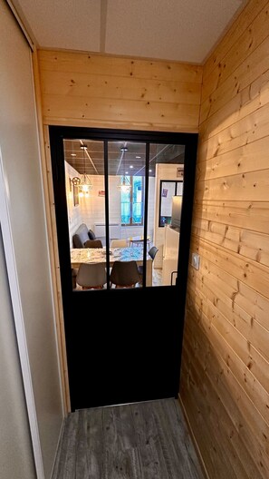 A wooden-paneled room with a black-framed door leading to a dining area with a table and chairs. - Family Apartment in La Bourboule (La Bourboule)