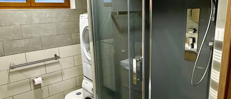 A modern bathroom with a glass-enclosed shower, a toilet, and a washing machine.