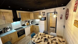 Una cucina moderna con mobili in legno, forno a incasso, microonde e lavandino. Sono presenti luci a sospensione e una decorazione murale a tema caffè.