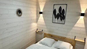 Una camera da letto con un letto di legno, biancheria bianca, un'opera d'arte appesa al muro e due luci fissate alla parete.