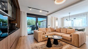 Una sala de estar moderna con un sofá seccional color beige, una mesa de centro y una zona de cocina con horno y microondas integrados.