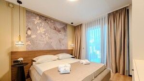 Habitación de hotel con una cama grande, cabecera con diseño floral, dos lámparas de noche y vista a la ciudad desde la ventana.