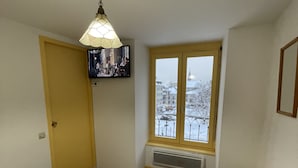 A bedroom with a bed, a television mounted on the wall, a window with a view of a snowy cityscape, and a small stool. - Bright Apartment in Mont-dore (Mont-Dore)