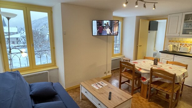 A living room with a sofa, a coffee table, and a TV mounted on the wall. - Bright Apartment in Mont-dore (Mont-Dore)