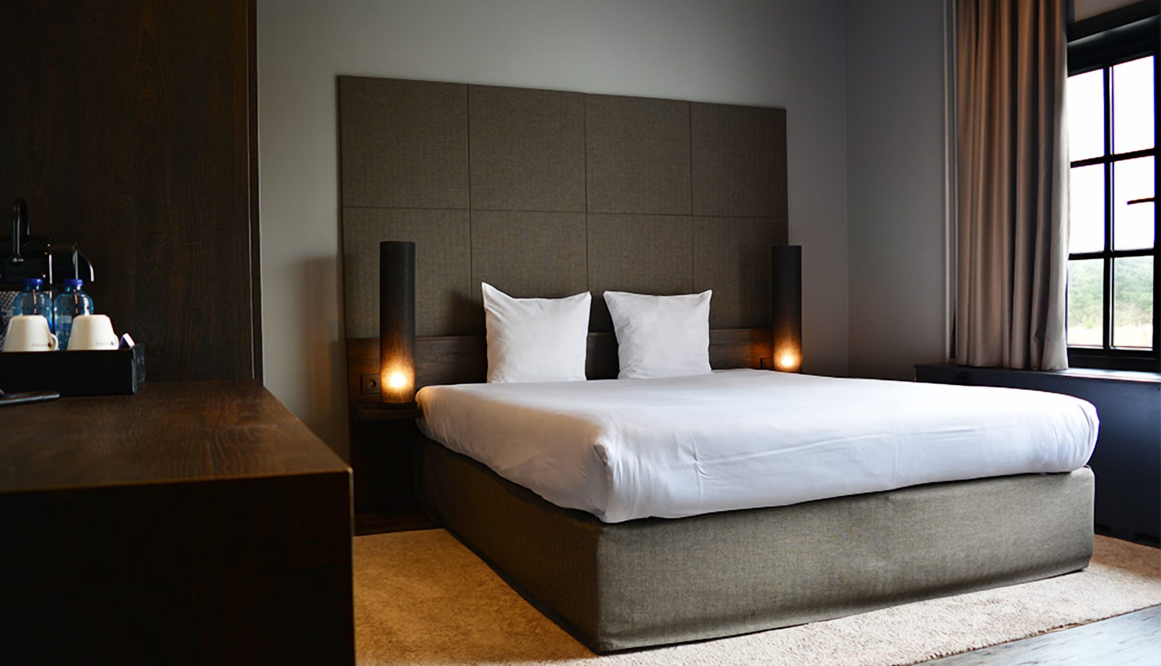 Ein modernes Hotelzimmer mit einem großen Bett, zwei Nachttischen, einem Fenster mit Vorhängen.