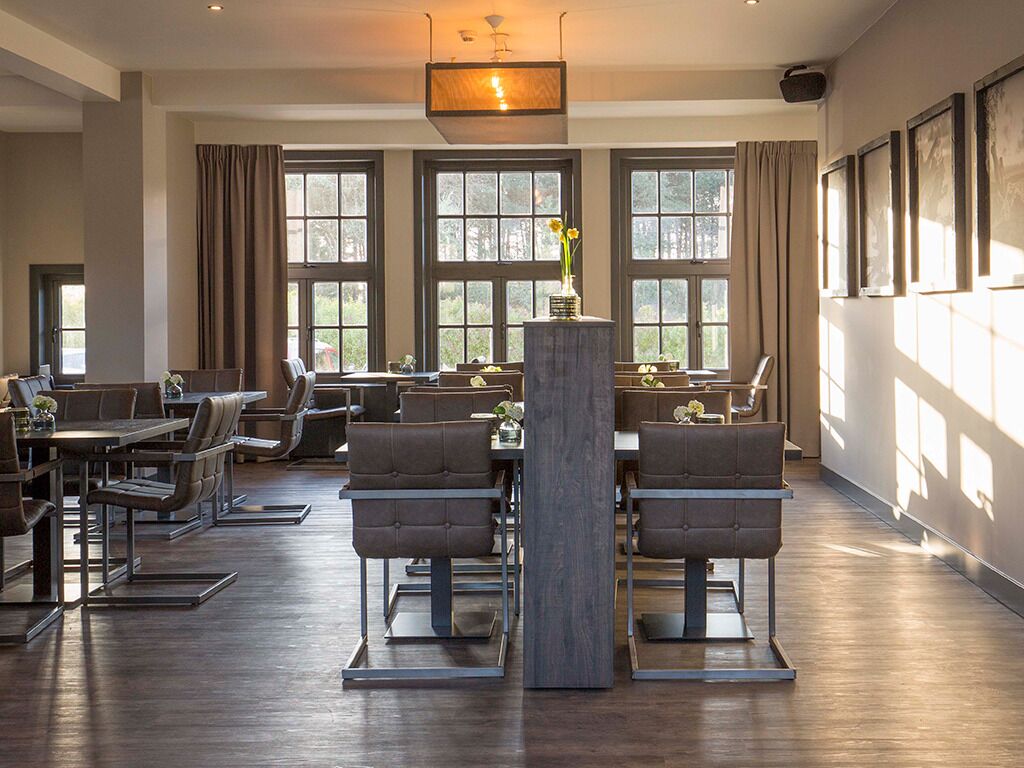 A spacious dining area with multiple tables and chairs, large windows with curtains, and a central decorative column.