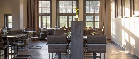 A spacious dining area with multiple tables and chairs, large windows with curtains, and a central decorative column.