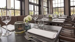 A dining area with tables set for a meal, large windows, and a view of greenery outside.