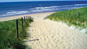 A sandy beach path leading to the ocean with a wooden fence on one side.