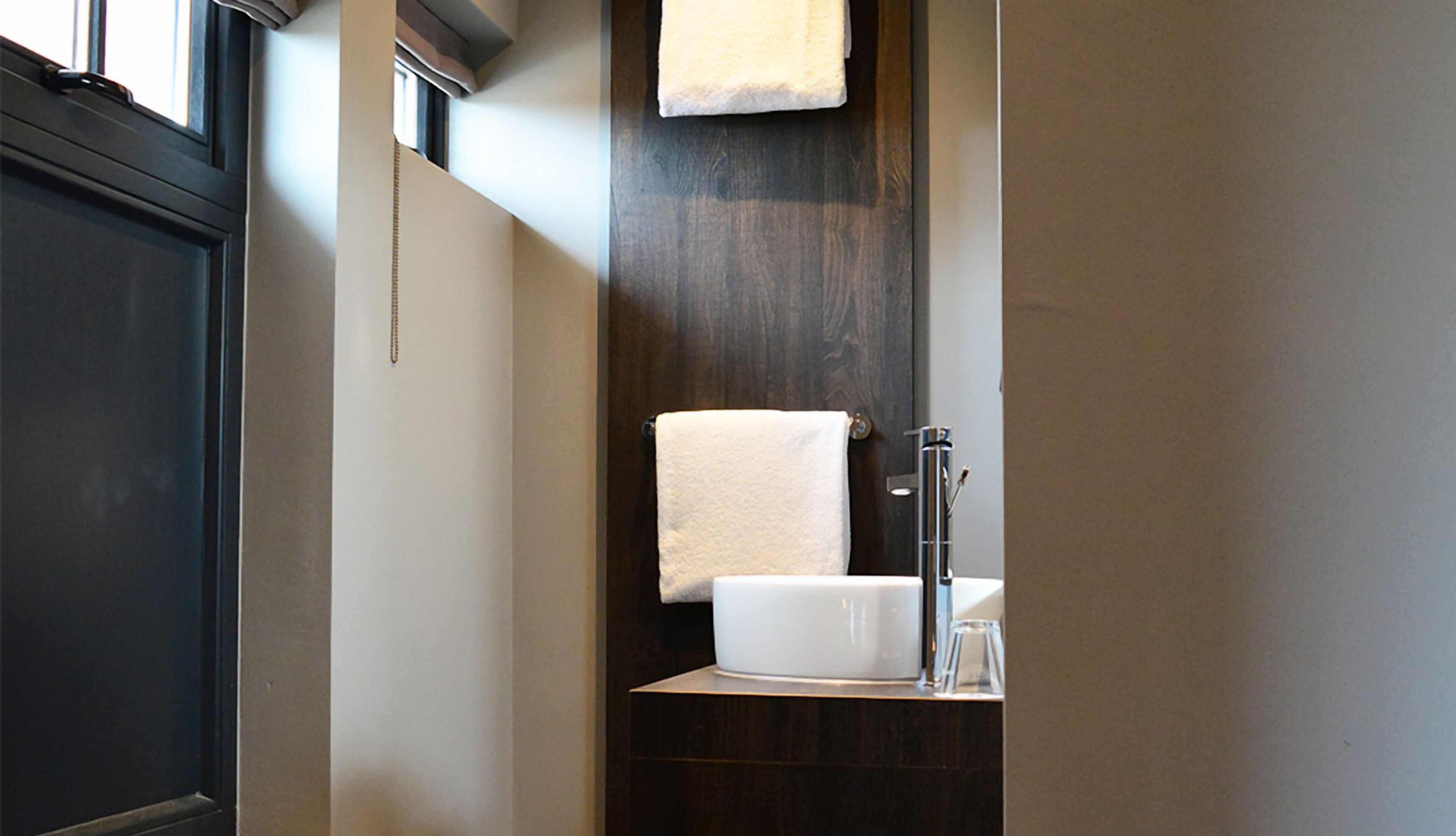 Un baño con tocador de madera oscura, un lavabo blanco y una toalla colgada en un perchero.