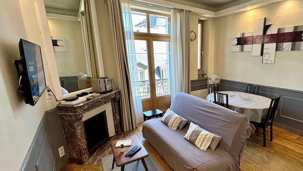 Ein Wohnzimmer mit einer Couch, einem kleinen Tisch, einem Kamin, einem Fernseher und einem Balkon mit Vorhängen.
