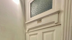 Eine weiße Tür mit kleinem Fenster darüber, ein Lichtschalter an der Wand und ein Klingel.