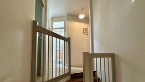 A narrow hallway with a wooden railing, a door leading to a room, and a light fixture on the ceiling. - Home for Groups and Families (Mont-Dore)