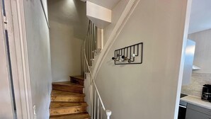 A staircase with wooden steps and white railings, leading to a landing with a wall-mounted light fixture. - Home for Groups and Families (Mont-Dore)