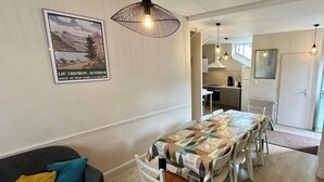 A modern kitchen with white cabinets, a dining table with a leaf-patterned tablecloth, and pendant lights. - Home for Groups and Families (Mont-Dore)