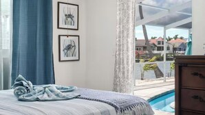 A bedroom with a bed, a window with a view of a pool and buildings, and two framed pictures on the wall. - ENDLESS SUMMER. Beautiful waterfront vacation home (Apollo Beach)