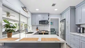 A modern kitchen with grey cabinets, a large island, and a view of the outdoors. - ENDLESS SUMMER. Beautiful waterfront vacation home (Apollo Beach)
