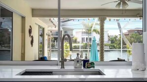 A modern kitchen with a large window overlooking a pool and buildings. - ENDLESS SUMMER. Beautiful waterfront vacation home (Apollo Beach)