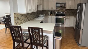 Una cucina moderna con mobili bianchi, un'isola centrale, elettrodomestici in acciaio inossidabile e un rivestimento a motivi decorativi.