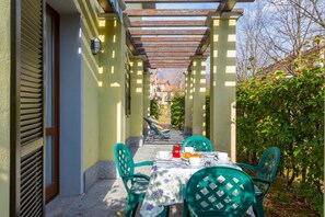 An outdoor patio with a table set for two, surrounded by green chairs, under a wooden pergola. - Mobilehome am Luganersee (Porlezza)