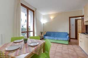 Un coin repas avec une table dressée pour deux personnes, un canapé vert et un espace cuisine avec des placards.