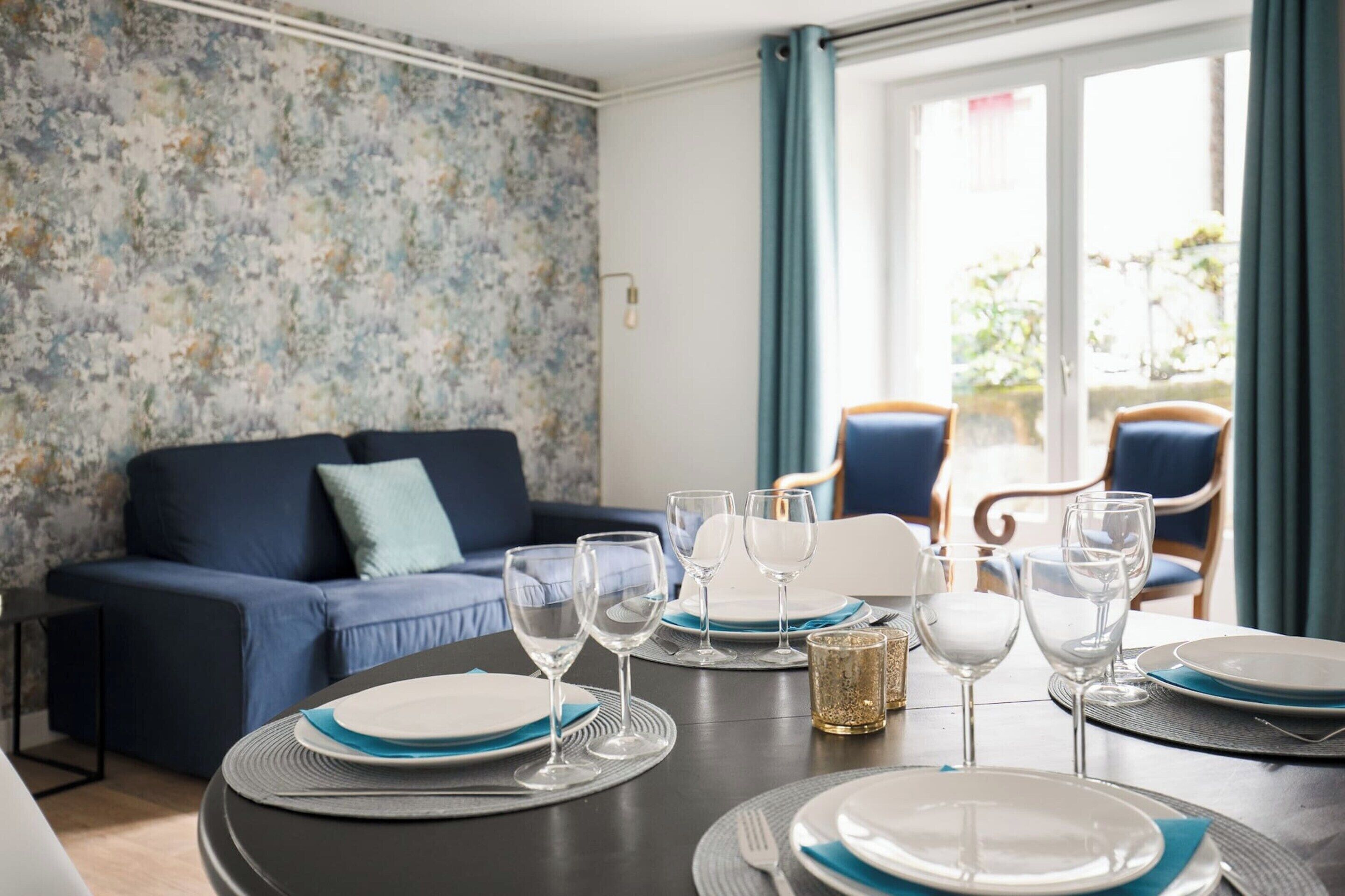 A dining area with a table set for four, a blue sofa, and a view of the outdoors.