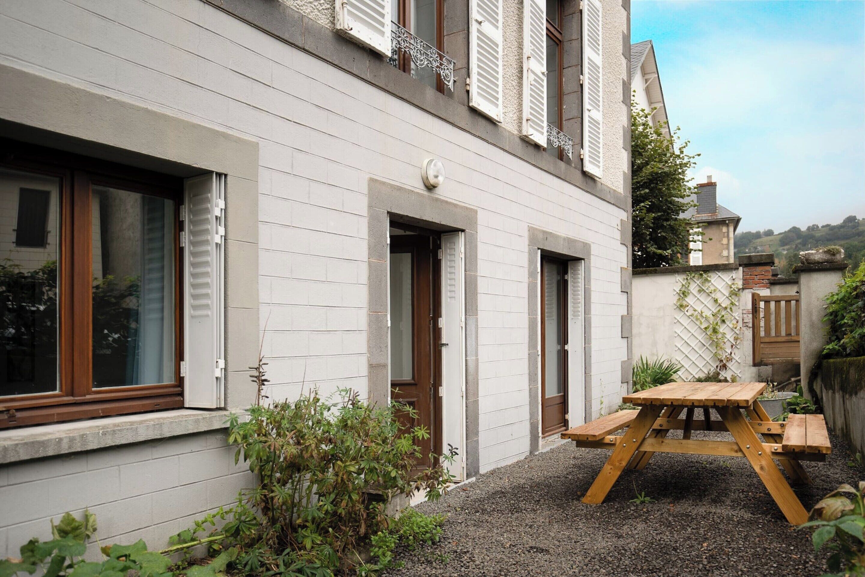 A building with a gravel patio, wooden picnic table, and a small garden area.