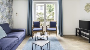 A living room with a sofa, two armchairs, a coffee table, a TV stand, and a large window with curtains. - La Bourboule Quiet Villa or 5 (La Bourboule)