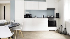 A modern kitchen with white cabinets, a black stove, and a dining area with white chairs and a round table. - La Bourboule Quiet Villa or 5 (La Bourboule)