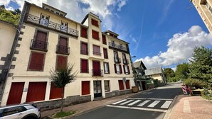 A multi-story building with red shutters and balconies, a clear sky, and a pedestrian crossing. - Modern 6-guest Flat in Mont-dore (Mont-Dore)