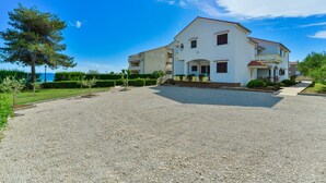 A two-story building with a gravel driveway, a small garden, and a clear blue sky. - Beachfront Apartment for 4 (Vir)