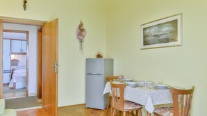 A dining area with a table set for four, a refrigerator, and a door leading to a bedroom. - Beachfront Apartment for 4 (Vir)