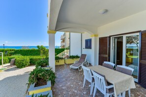 A covered outdoor patio with a table and chairs, a view of the sea, and a staircase leading to a balcony. - Beachfront Apartment for 4 (Vir)