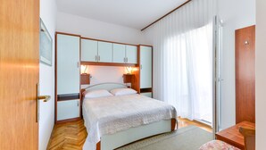 A bedroom with a bed, wooden wardrobe, bedside lamps, and a window with curtains. - Beachfront Apartment for 4 (Vir)