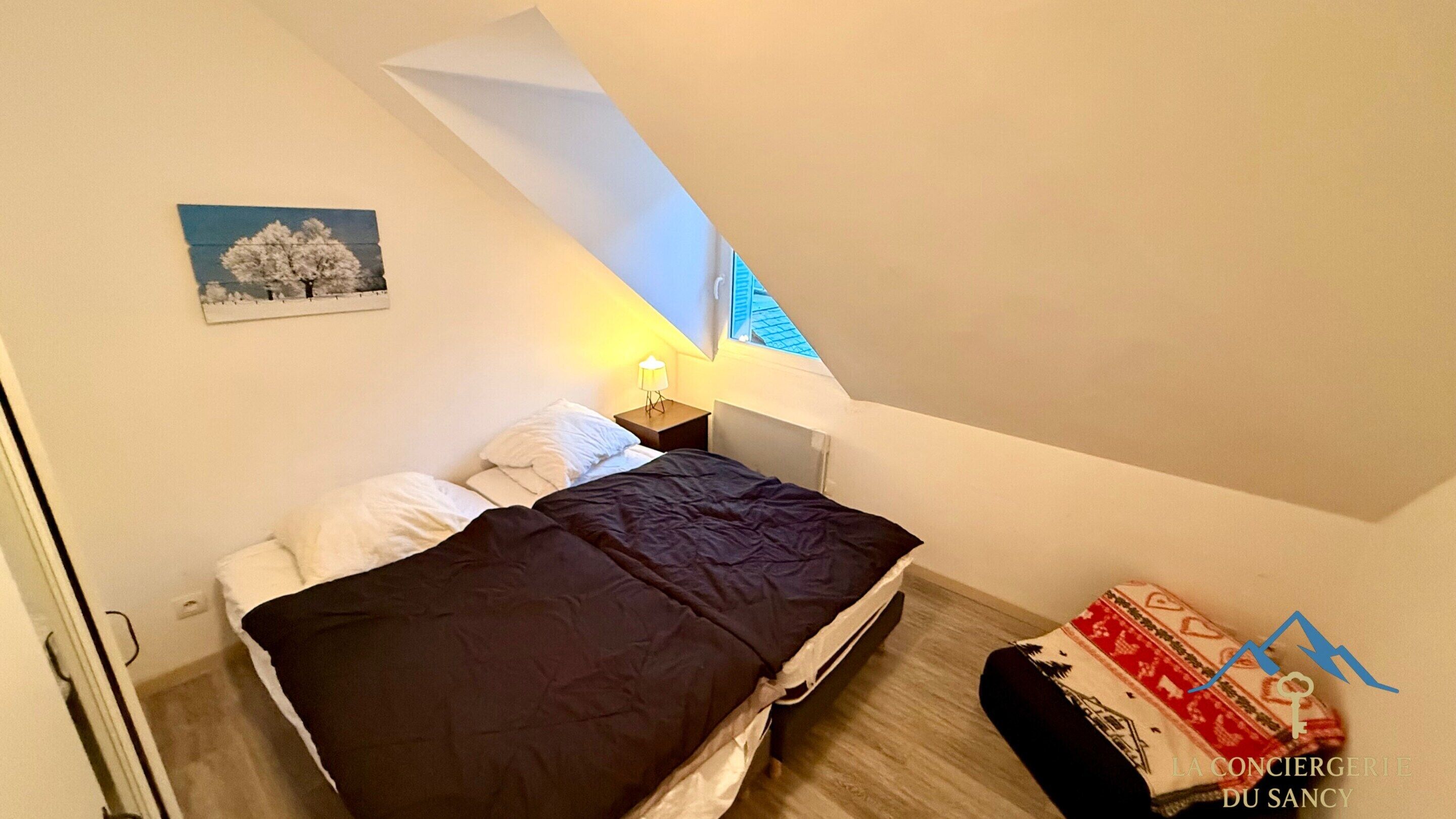 A bedroom with a bed, a nightstand, a lamp, a picture on the wall, and a window with a view of a building.