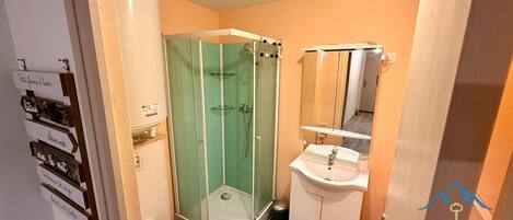 Une salle de bain avec une douche à parois de verre, un lavabo blanc et un miroir au-dessus du lavabo.