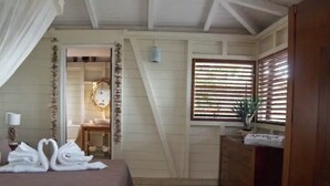 Een slaapkamer met een bed, een nachtkastje, een raam met zonwering en een deur naar een andere kamer.