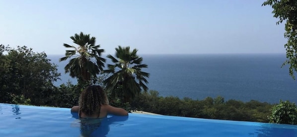 A person relaxing in a pool with a view of the ocean and palm trees.